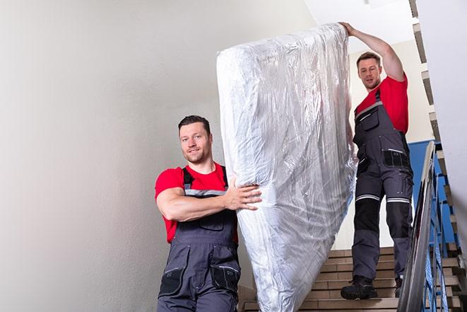 two people carrying a box spring down a staircase in Burnet